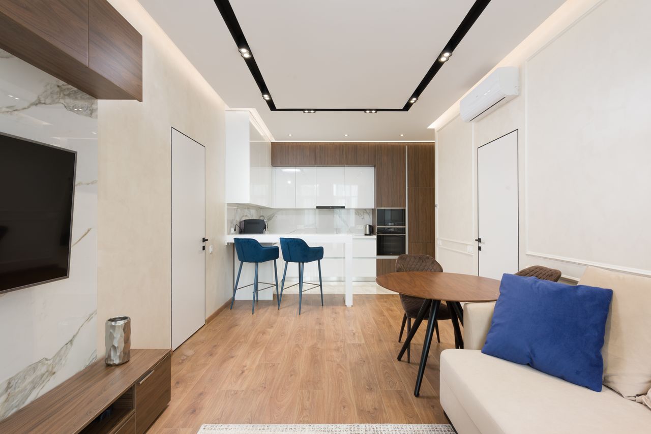 services-img Interior of modern apartment with living room with comfy sofa and wooden furniture near kitchen zone with counter and white cabinets