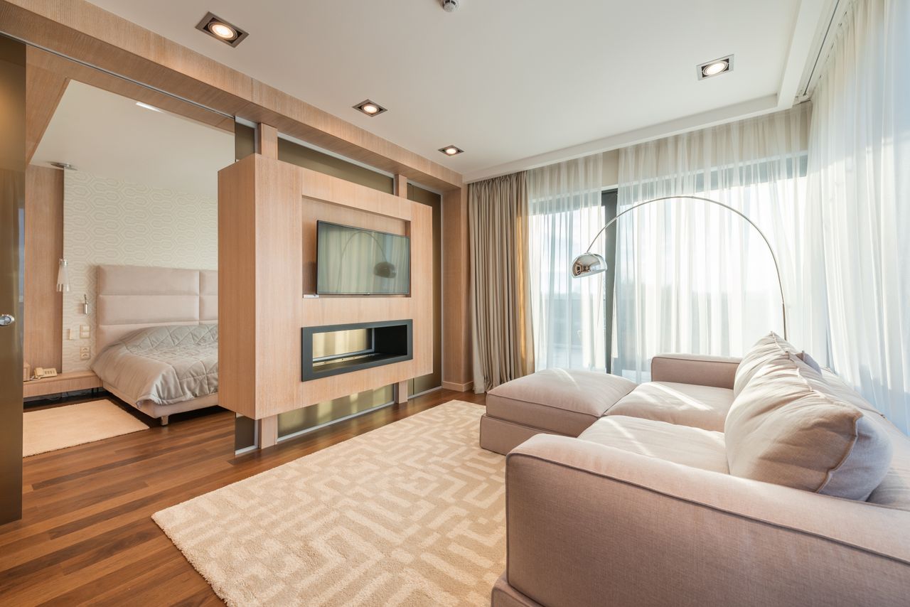 services-01 Interior of modern apartment with comfortable couch with pillows on carpet against TV in living room near bedroom with bed